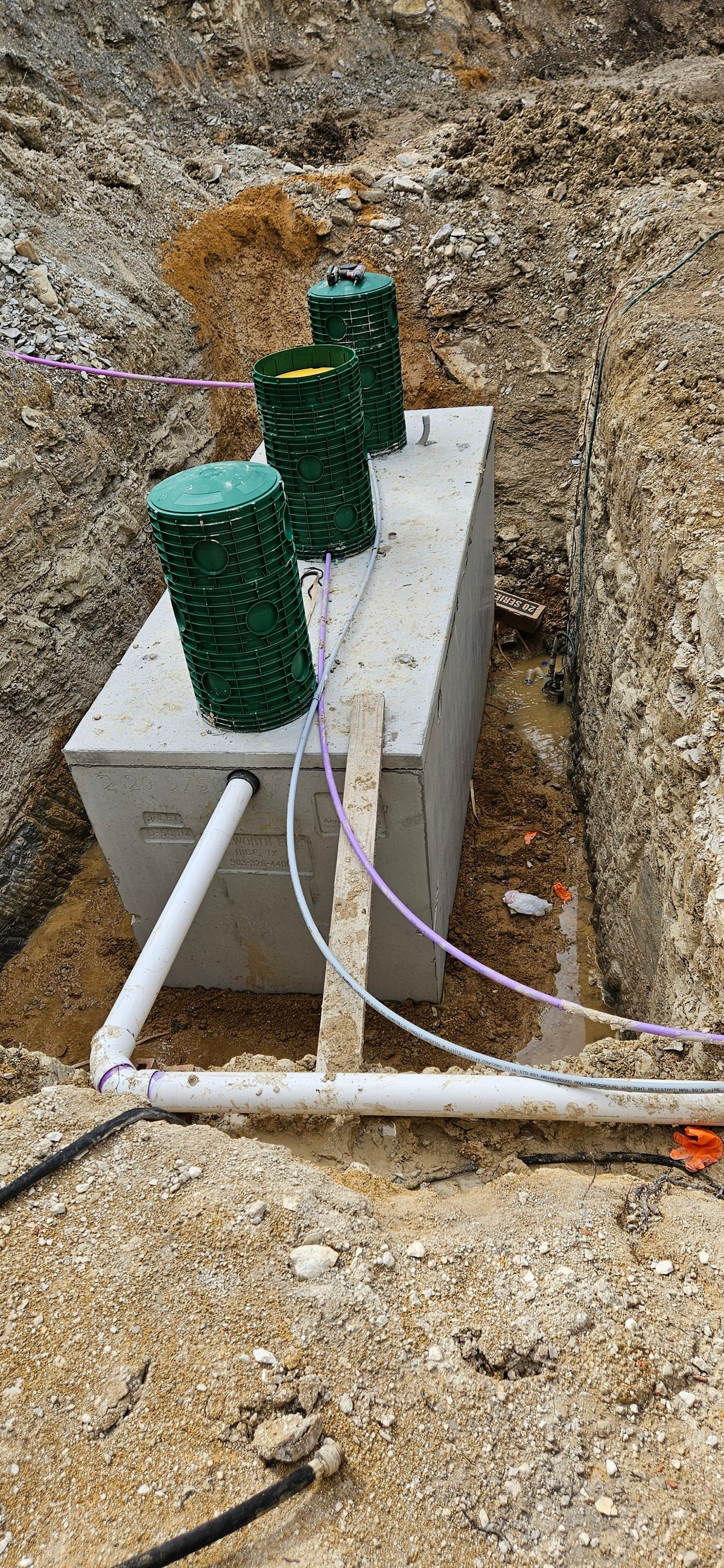 Septic system installation in excavated ground with concrete tank and green water storage barrels connected by pipes