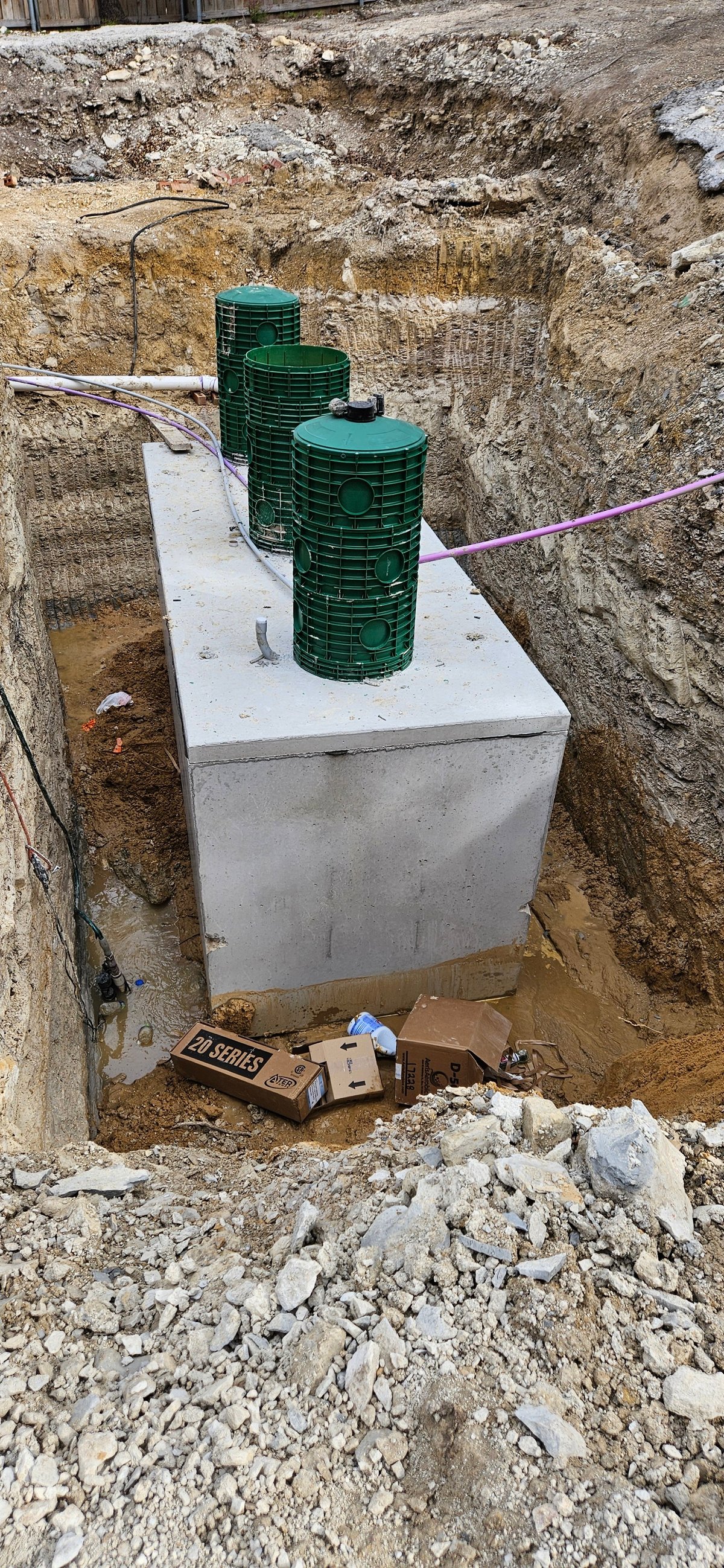 Three green septic tanks stacked on a concrete foundation in an underground installation pit with wiring visible