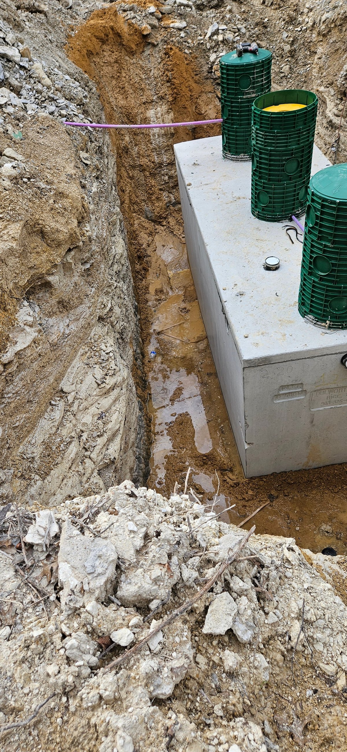 Septic system installation in excavated hole with white tank and green storage tanks aboveground